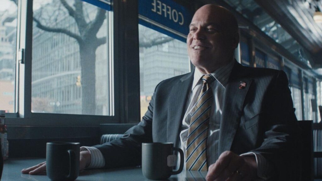 20 Absolutely Best TV Shows to Watch Right Now (June 2025) 69 Wilson Fisk sitting in a diner, smiling, with two coffee mugs placed in front of him on a table.
