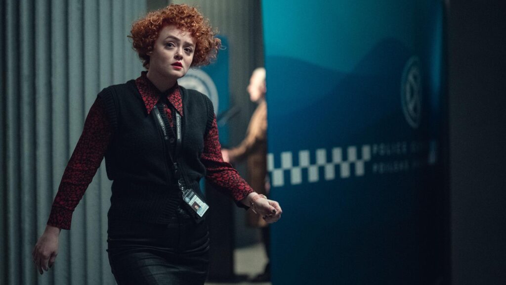 20 Absolutely Best TV Shows to Watch Right Now (June 2025) 77 DC Rose Dickson (Leah Byrne) wearing a dark outfit with red patterned sleeves and a black vest walks through a modern office corridor.