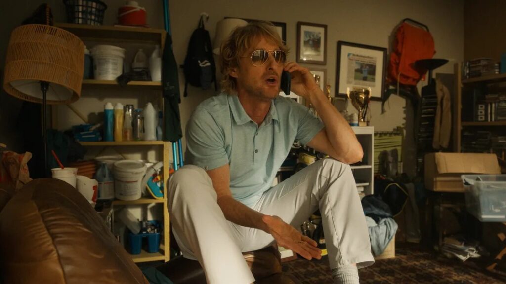 20 Absolutely Best TV Shows to Watch Right Now (June 2025) 90 Pryce Cahill (Owen Wilson) in sunglasses talks on a phone while sitting in what appears to be a cluttered storage room or garage.