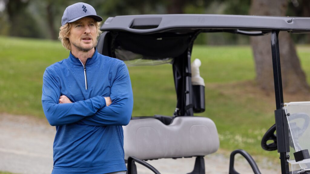 20 Absolutely Best TV Shows to Watch Right Now (June 2025) 86 Pryce Cahill (Owen Wilson) in blue golf attire and cap stands with arms crossed next to a golf cart on a golf course.