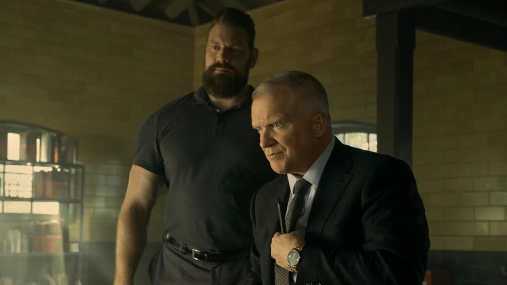 20 Absolutely Best TV Shows to Watch Right Now (June 2025) 93 Paulie in dark clothing stands behind Zachary Beck in a business suit.