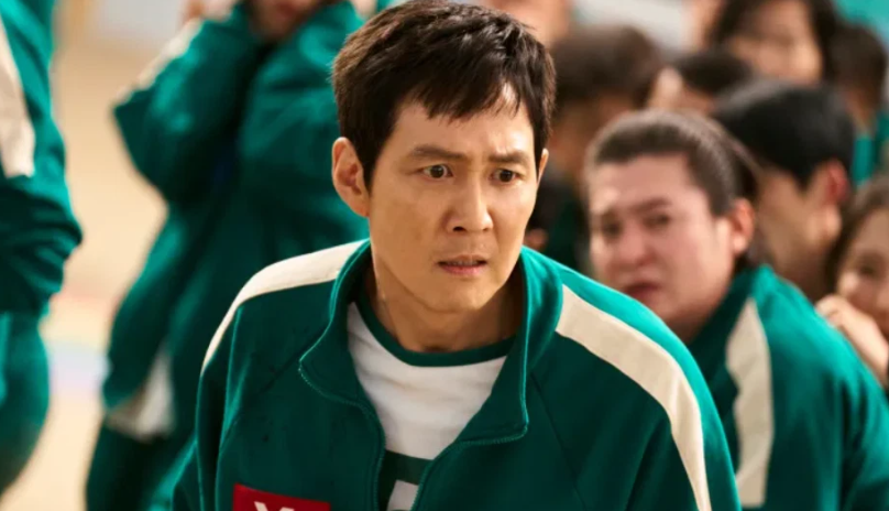 What You Need to Know About Player 456 Ahead of ‘Squid Game’ Season 3 4 Seong Gi-hun looks scared and confused in a room full of other people in green tracksuits.