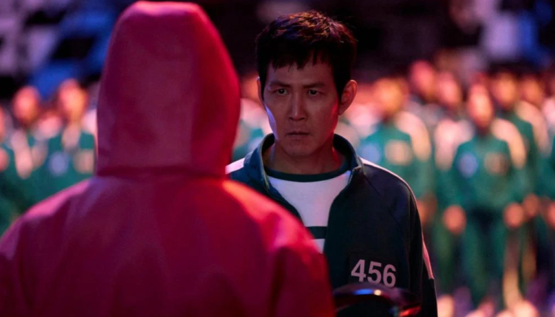 What You Need to Know About Player 456 Ahead of ‘Squid Game’ Season 3 6 Seong Gi-hun in Squid Game stares seriously at a person in a pink suit.