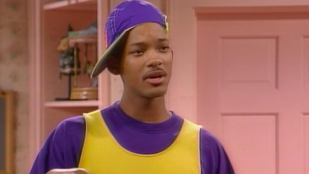 10 Insanely Popular TV Shows From the ‘90s You Can Stream on Netflix 15 Will Smith as the Fresh Prince in his signature colorful '90s outfit - purple and yellow shirt with backwards cap - standing against a pink background in the Banks family home.