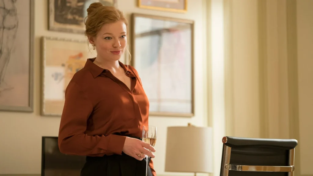 9 Things You Did Not Know About ‘Succession’ Star Sarah Snook 3 Sarah Snook in a brown blouse holding a glass of champagne in hand.