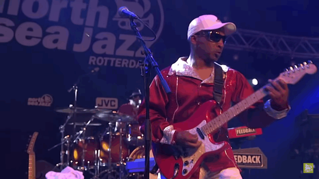 Sly Stone Dies at 82: What We Know About His Wife, Family, and Net Worth 8 Sly Stone in a red shirt and white cap performing on stage with a red electric guitar live at North Sea Jazz 2007.