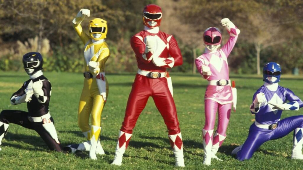 10 Insanely Popular TV Shows From the ‘90s You Can Stream on Netflix 30 Outdoor action scene from "Mighty Morphin Power Rangers" showing the five original Rangers (Black, Yellow, Red, Pink, and Blue) in their suits performing martial arts poses on a grassy field.