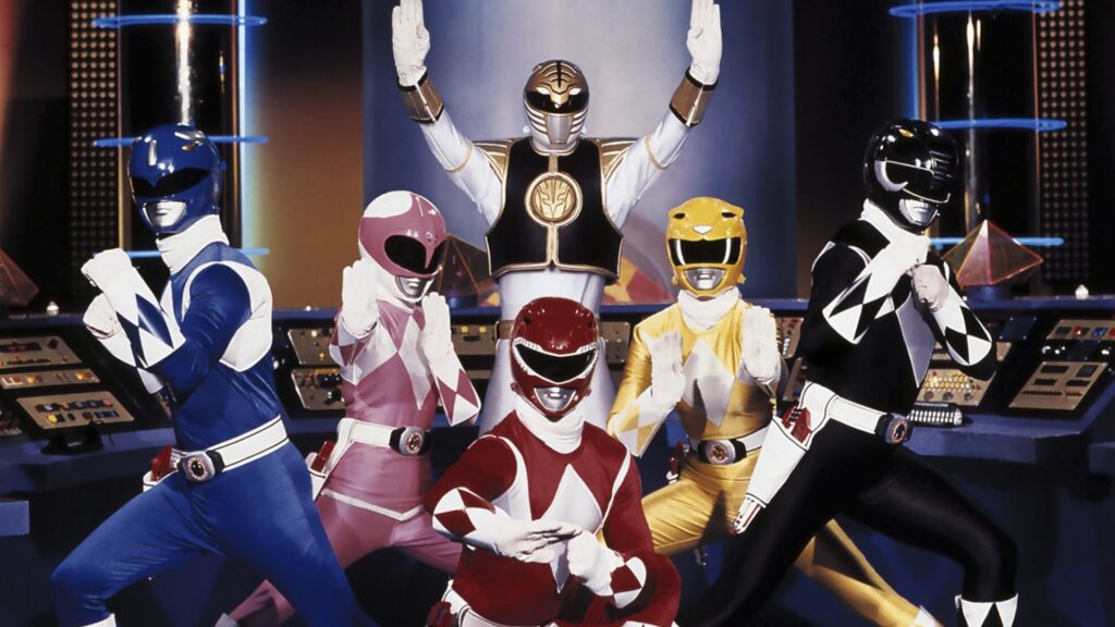 10 Insanely Popular TV Shows From the ‘90s You Can Stream on Netflix 26 Group shot from "Mighty Morphin Power Rangers" showing all six Rangers in their full colored suits and helmets (Blue, Pink, White, Red, Yellow, and Black) posed in their Command Center with futuristic control panels visible in the background.