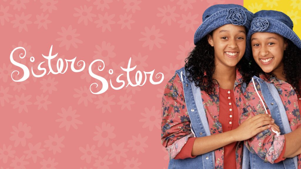10 Insanely Popular TV Shows From the ‘90s You Can Stream on Netflix 36 Promotional image for "Sister, Sister" TV show featuring Tia and Tamera in matching denim outfits and hats standing close together against a coral pink background, with the show's title in white cursive lettering.