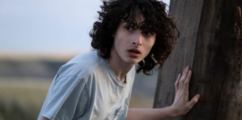 How Old Is ‘Stranger Things’ Cast: Actors’ Age in Season 1 and Season 5 2 Mike Wheeler is wearing a light blue t-shirt and he looks surprised or worried, with his hand resting on a tree.