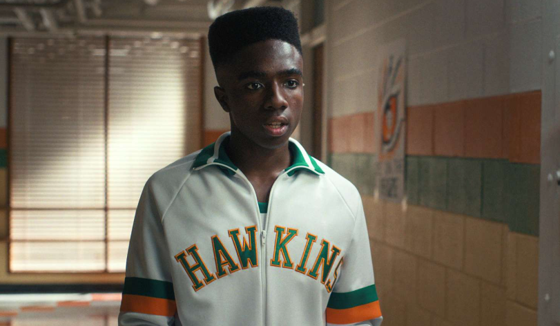 How Old Is ‘Stranger Things’ Cast: Actors’ Age in Season 1 and Season 5 5 Lucas Sinclair with a high-top haircut is wearing a white and green track jacket. He is standing indoors, in a school hallway.