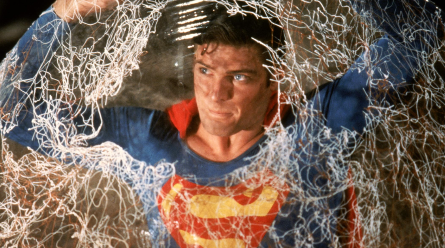 Superman is entangled in a white net. He is trying to break free.