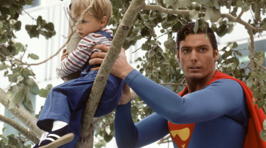 Superman, in his iconic suit, carefully rescuing a small child who is sitting in a tree.
