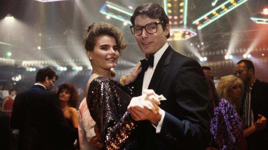 Clark Kent is dancing with Lacy at a lively party or disco. Both are smiling and looking at the camera.