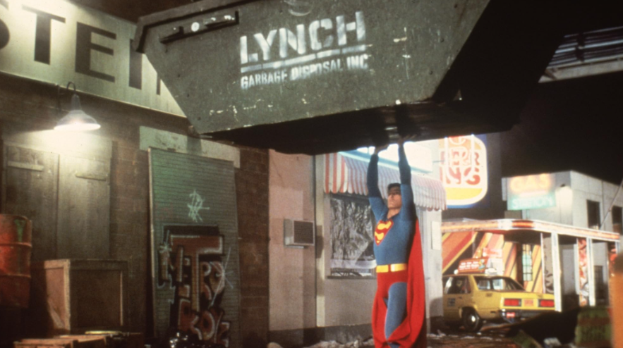 Superman is holding up a large garbage dumpster.