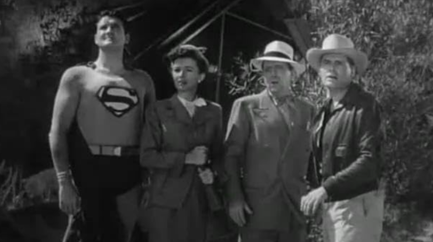 Superman stands tall, looking up, next to a woman and two men in hats.