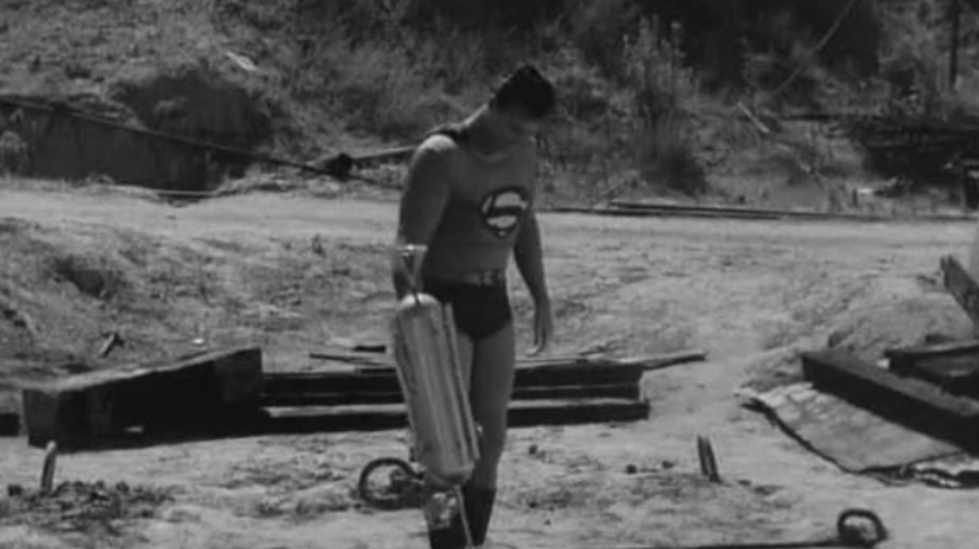 Superman is trying to pull up a large, cylindrical object.