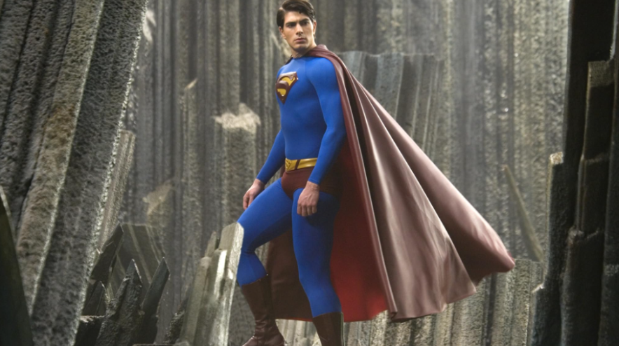 Superman, in his blue and red suit with a flowing cape, stands powerfully on a rocky setting.