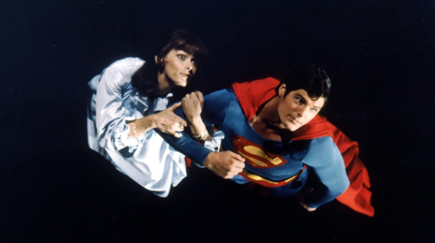 Superman is seen flying upwards, holding Lois Lane.