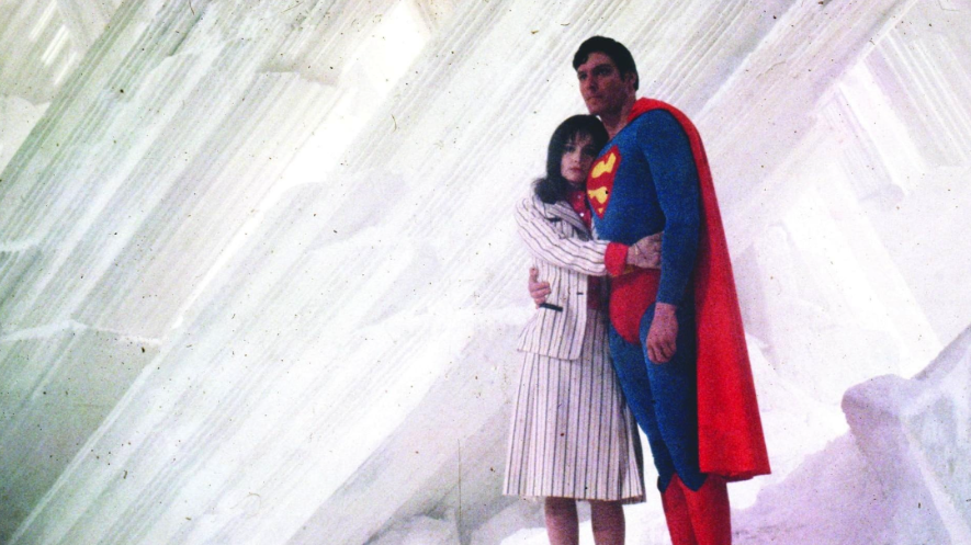 Superman stands embracing a Lois, both looking to the right in a crystal-like environment.