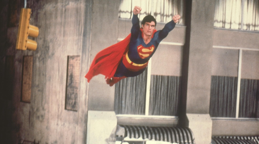Superman is flying through the air with his arms raised.