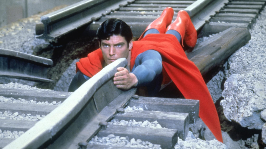 Superman is seen lying on train tracks, as if he's trying to stop or prevent something from happening.