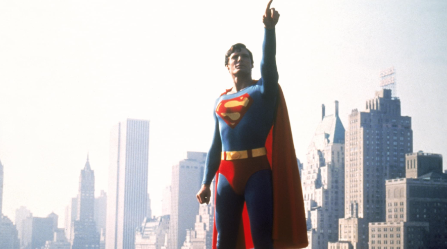 Superman stands tall against a city skyline, pointing heroically upwards.