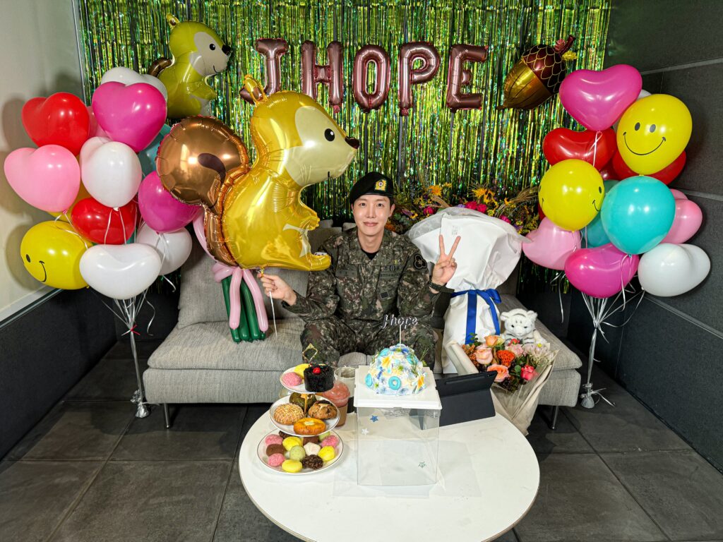 J-Hope sitting on a couch with his military uniform surrounded by decoration to celebrate his discharge day