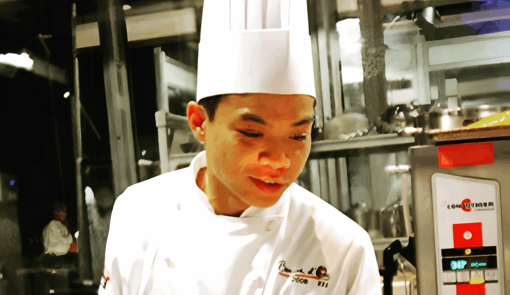 All 21 ‘Top Chef’ Winners and How Their Life Looks Like Today After Winning the Prize Money 3 Hung Huynh in white traditional chef's hat and coat working intently in a professional kitchen.