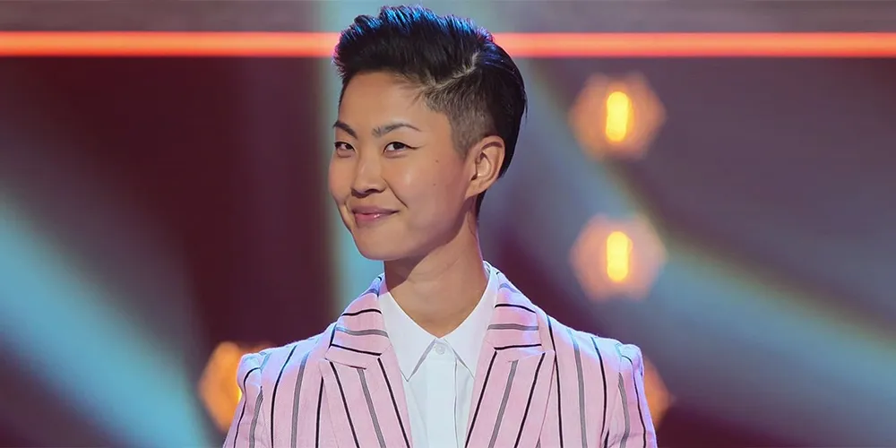 All 21 ‘Top Chef’ Winners and How Their Life Looks Like Today After Winning the Prize Money 10 Kristen Kish in pink and white striped blazer with short dark hair, smiling at camera against colorful stage lighting background of "Iron Chef."
