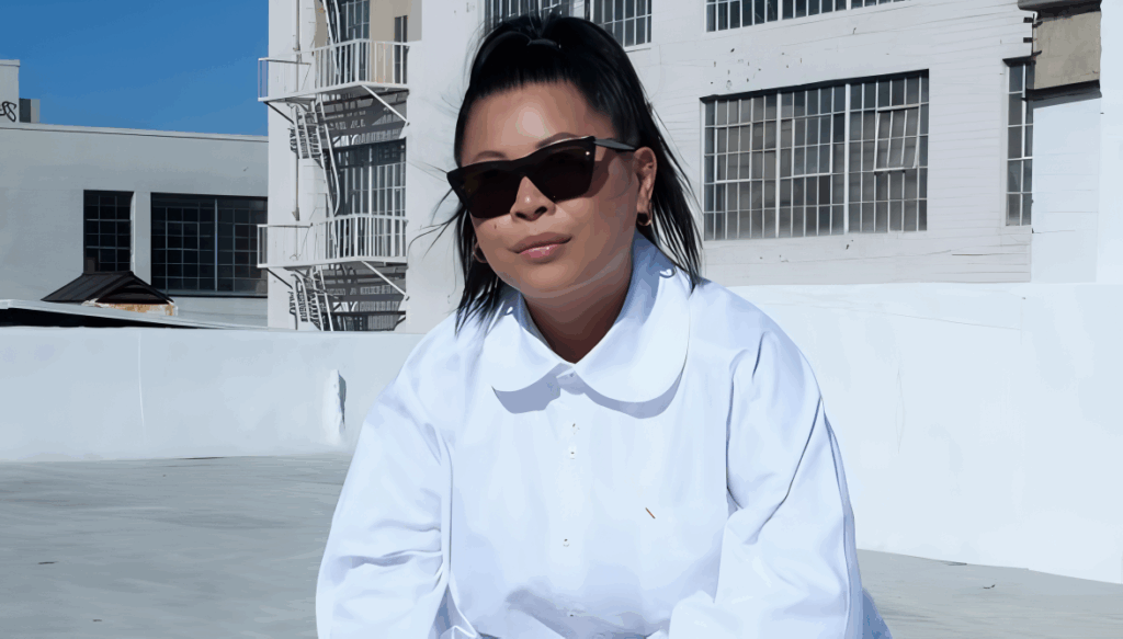 All 21 ‘Top Chef’ Winners and How Their Life Looks Like Today After Winning the Prize Money 12 Mei Lin in white chef's coat and sunglasses, posing on a rooftop with urban buildings in the background.