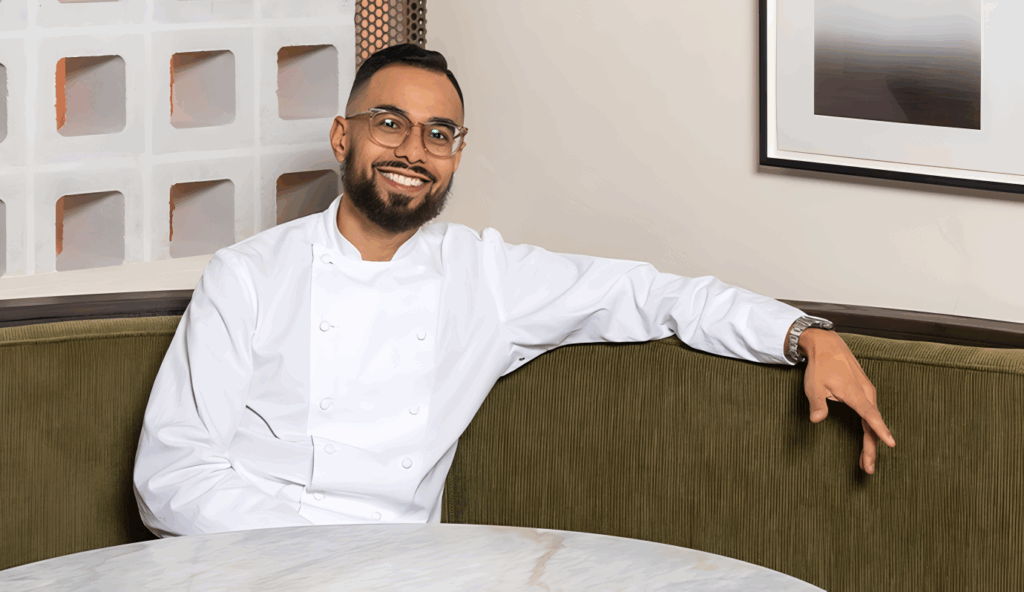 All 21 ‘Top Chef’ Winners and How Their Life Looks Like Today After Winning the Prize Money 20 Smiling Danny Garcia with glasses and beard in white chef's coat, sitting relaxed in a restaurant booth.