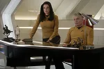 A still from Star Trek: Strange New Worlds Season 3 featuring Una and Pike standing behind and sitting at a desk respectively.