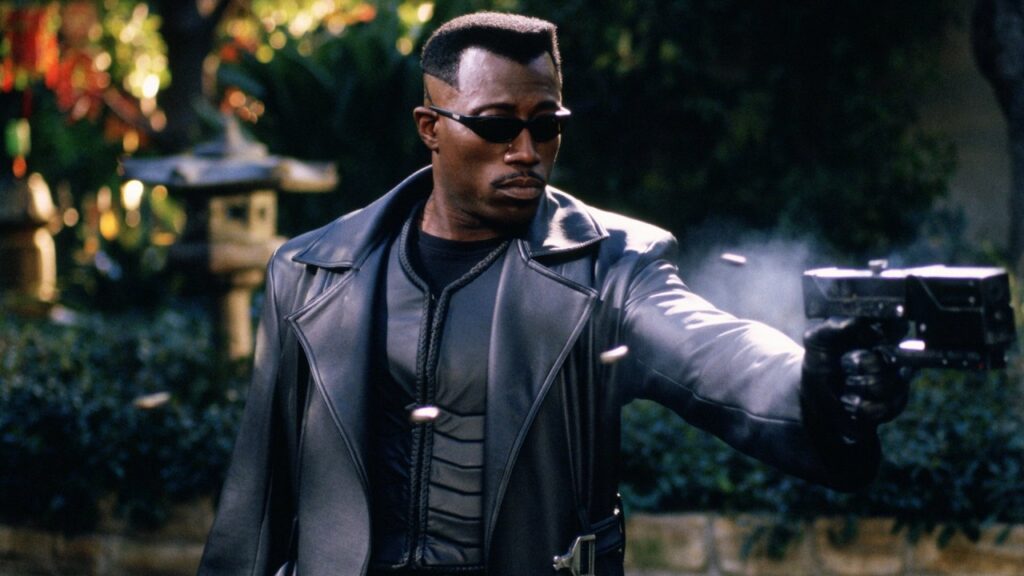 Original ‘Blade’ Writer Hasn’t Given Up on Mahershala Ali Despite Being “99% done” With Superheroes 1 Wesley Snipes wearing leather jackets, shades, and wielding a gun in his left hand in Blade.