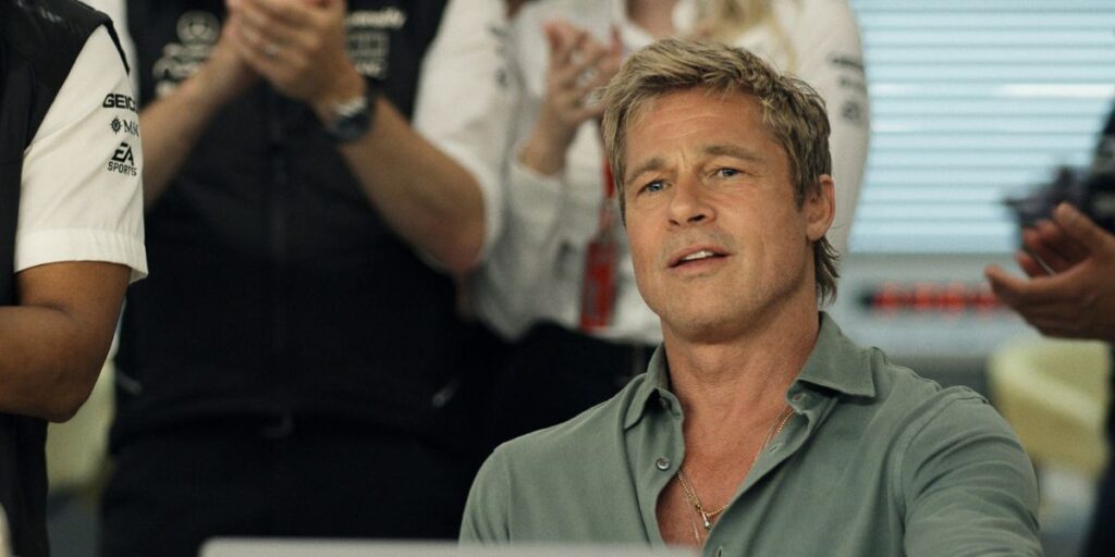 Brad Pitt as Sonny Hayes sitting infront of a computer screen as people clap behind him in F1 The Movie