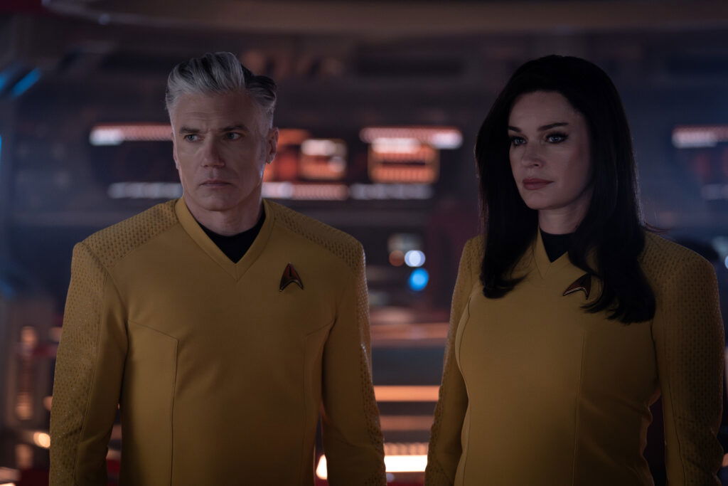 A still from Star Trek: Strange New Worlds Season 3 featuring Pike and Una standing in front of several computer monitors