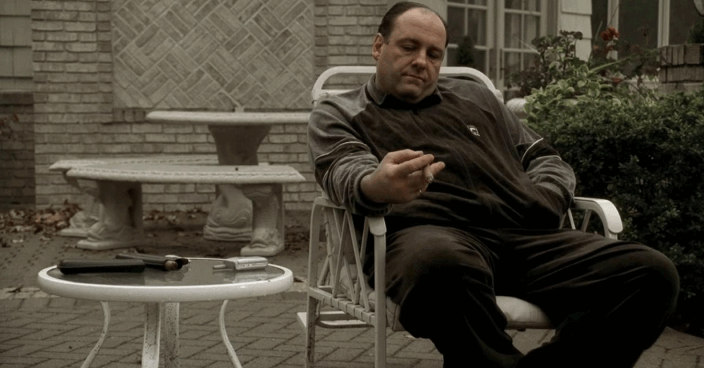 10 Best The Sopranos Episodes That Makes It Better Than Breaking Bad 5 Tony smoking a cigar sitting on a lawn chair.