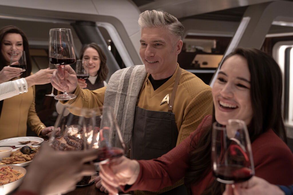 A still from Star Trek: Strange New Worlds Season 3 featuring Una, Batel, Pike, and La'an celebrating and drinking wine.