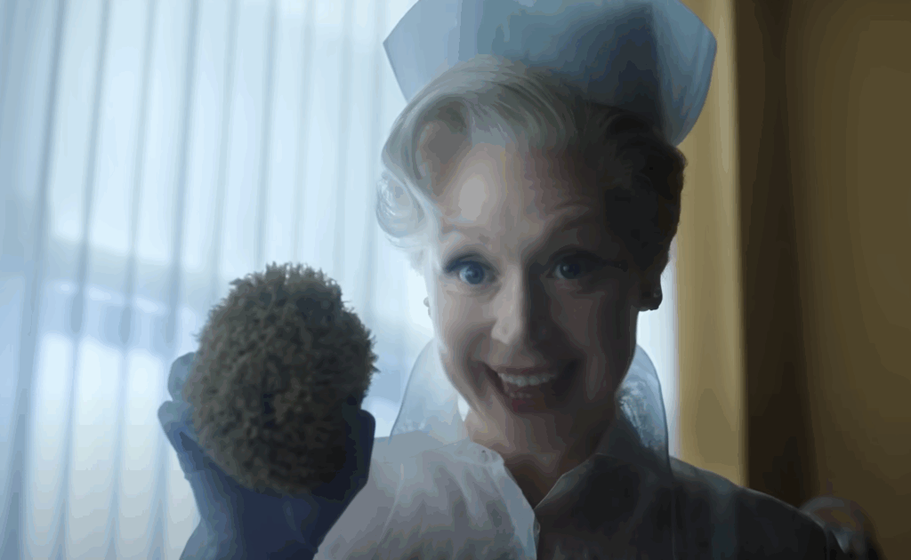 Principal Larissa, dressed as a nurse, holding a sponge in Wednesday. 