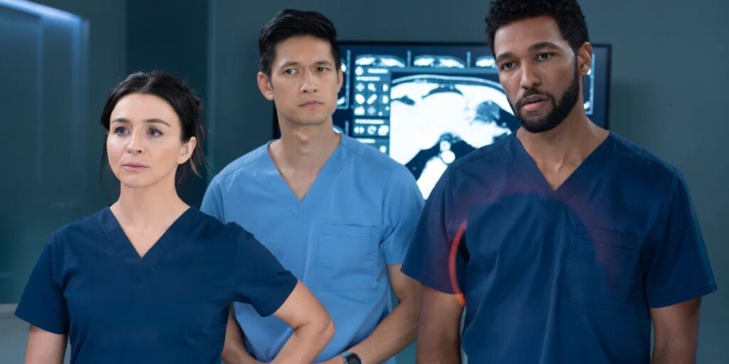 Caterina Scorsone, Harry Shum Jr., and Anthony Hill standing side-by-side looking concerned in their doctor's scrubs in the hospital in Grey's Anatomy