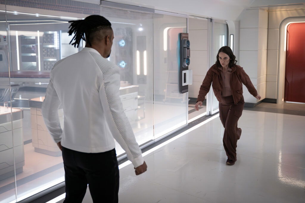 A still from Star Trek: Strange New Worlds Season 3 featuring Batel rushing at Gamble, whose back is turned to the camera