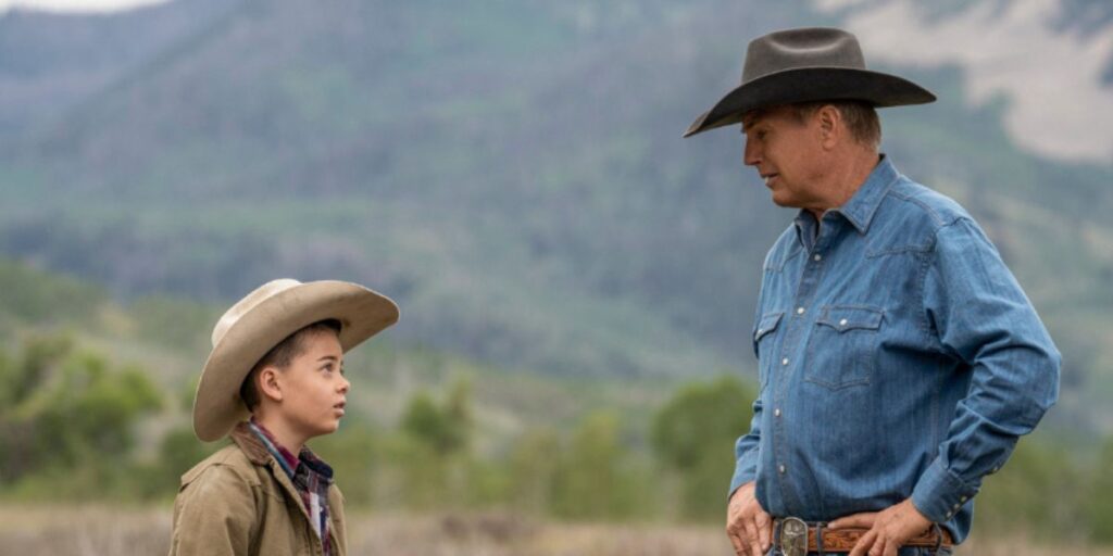 Brecken Merrill as Tate Dutton and Kevin Costner as John Dutton in Yellowstone talk in an open field