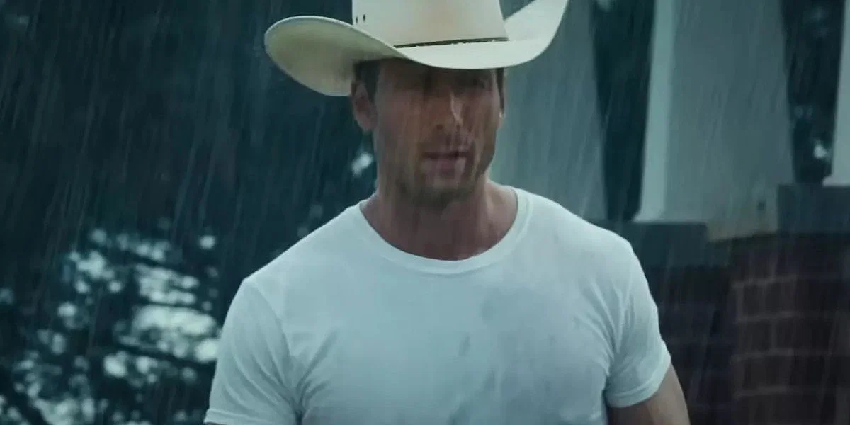 Glen Powell in Twisters drenched in rain and wearing a white t-shirt with a white cowboy hat