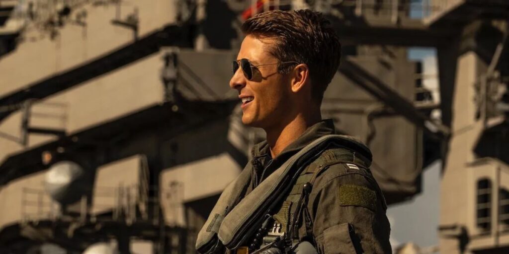 Side profile of Glen Powell from waist-up. He is wearing glasses and is in an airforce attire.
