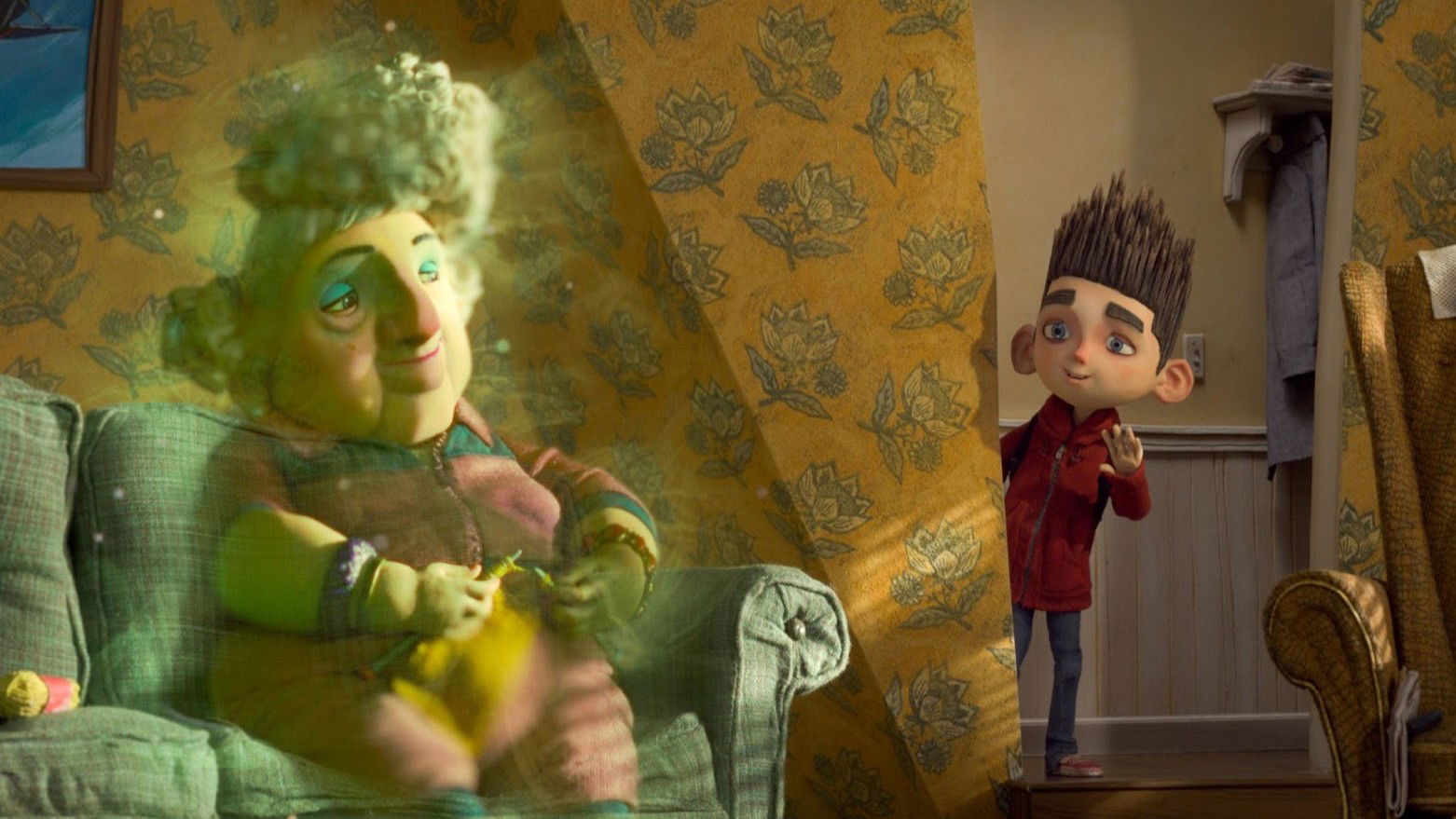 Grandma Babcock with curly gray-green hair sits in a green armchair, glowing with a mystical light, while Norman in a red sweater watches from nearby in a warmly decorated room.