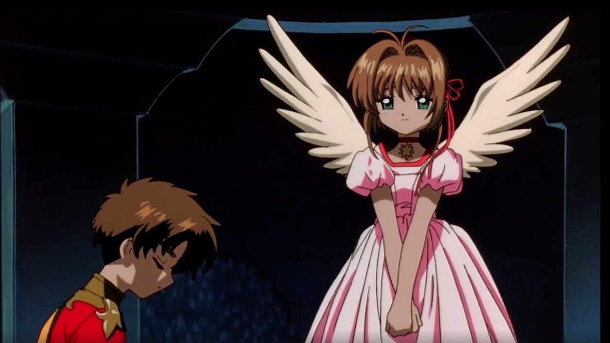 Sakura Kinomoto with brown hair wearing a pink and white dress with large white wings, standing next to Syaoran Li in darker clothing against a black background and kneeling.
