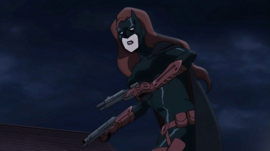 Batwoman in a dark costume with red accents, holding two weapons while positioned on a rooftop against a night sky.