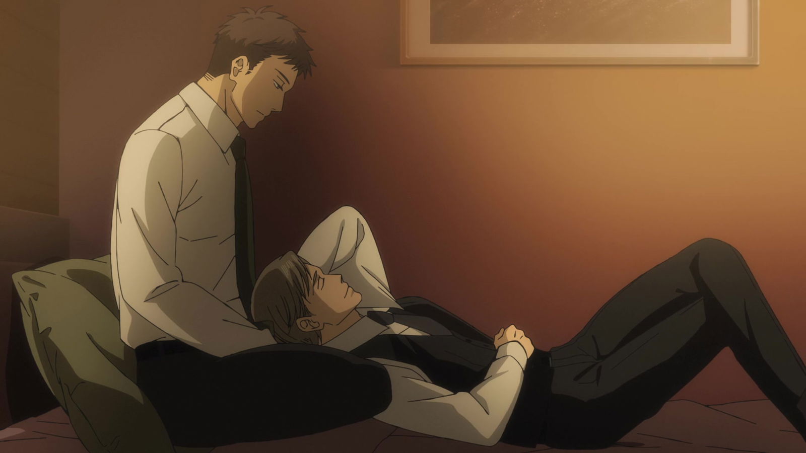 An intimate indoor scene showing two young men on a bed in warm lighting. One sitting up, one lying down, suggesting a quiet personal moment.