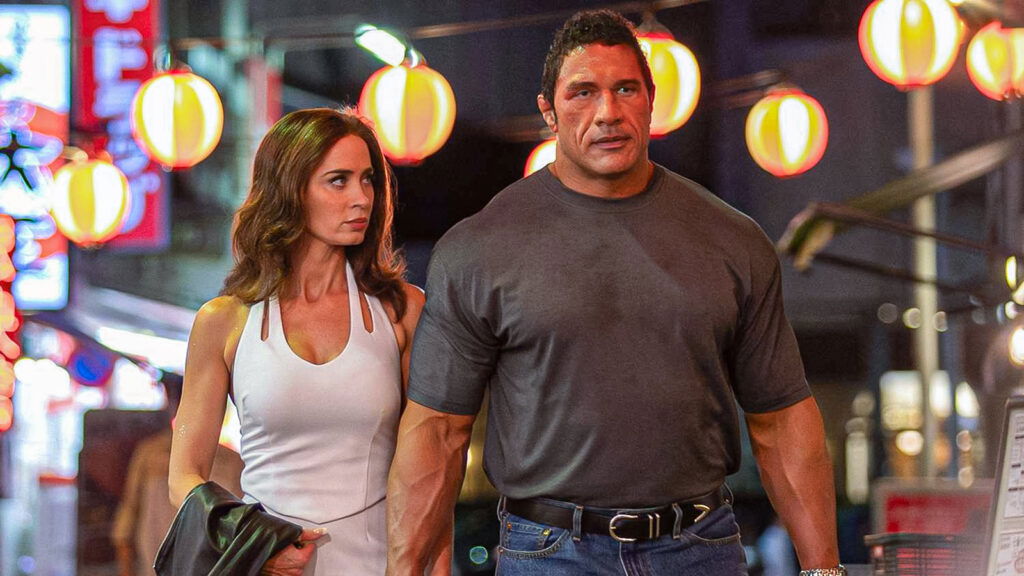 Emily Blunt walking alongside Johnson's Mark Kerr in a fair in The Smashing Machine