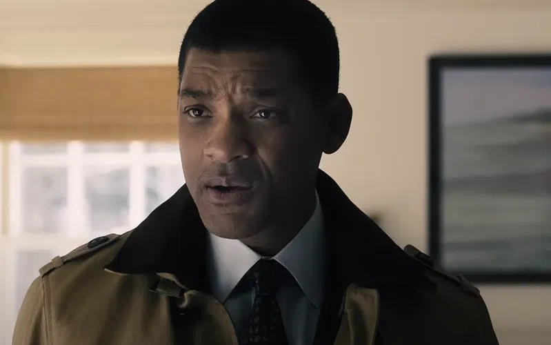 Will Smith in a khaki colour coat, a suit, and a tie.